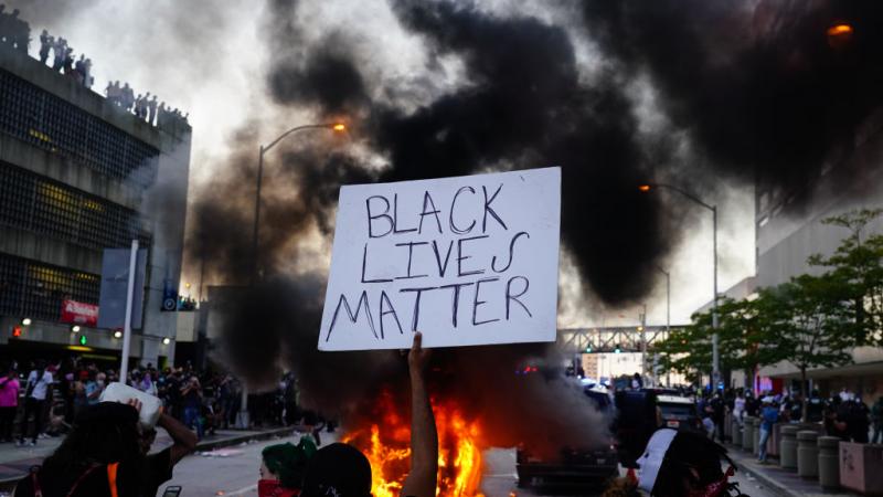 Person holds Black Lives Matter sign as police car burns in Georgia in May 2020