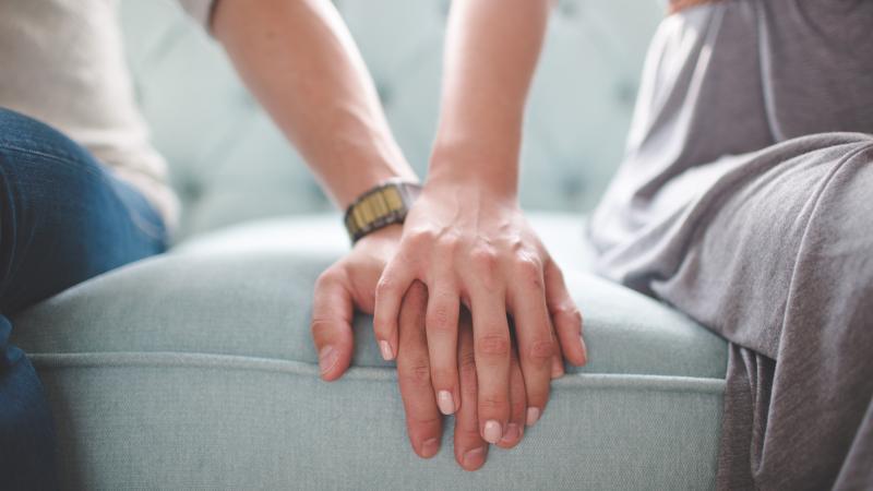 Man, woman holding hands on coach