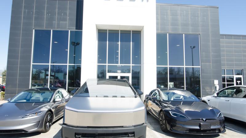 Tesla cars are displayed at a dealership in Westmont, Illinois, as protesters demonstrate against Elon Musk in the background, in Chicago